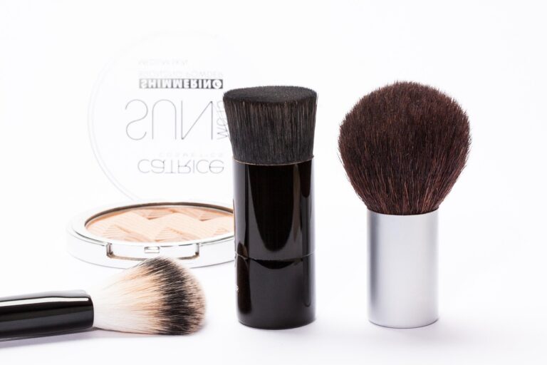 Drei Make-up-Pinsel und eine offene Puderdose auf weißem Hintergrund.