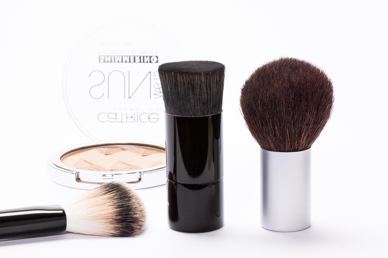 Drei Make-up-Pinsel und eine offene Puderdose auf weißem Hintergrund.