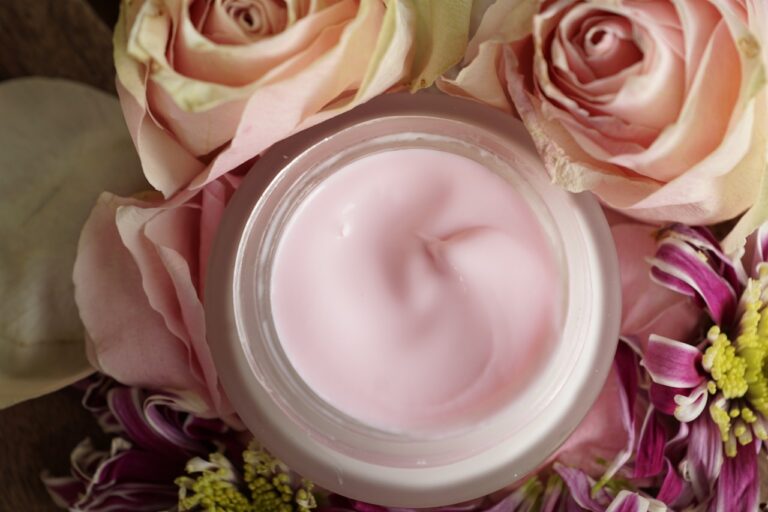 Offenes Glas mit rosa Creme, umgeben von verschiedenen Blumen.