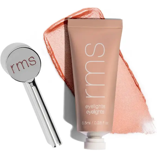 Lidschatten-Tube neben silbernem Applikator vor peachfarbenem Streifen.